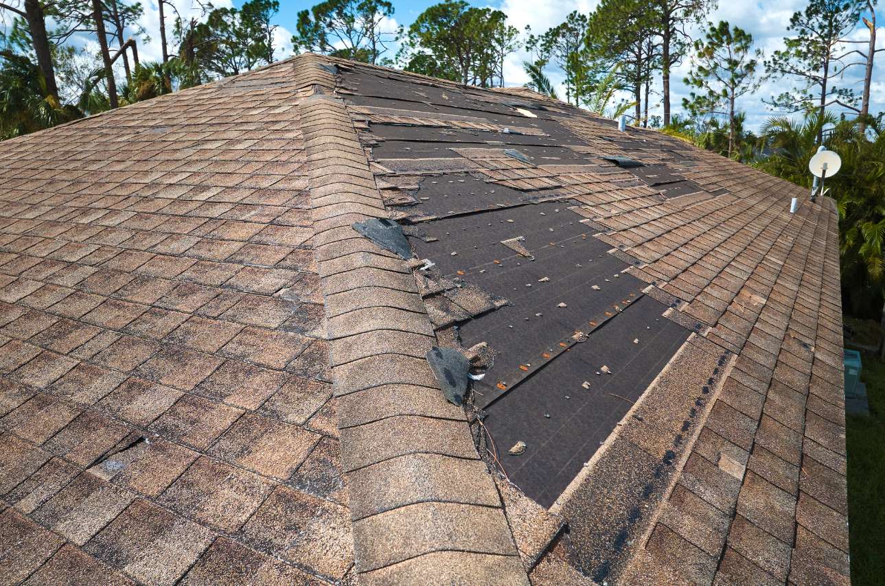 Brown roof with missing shingles and other visible damage after a storm